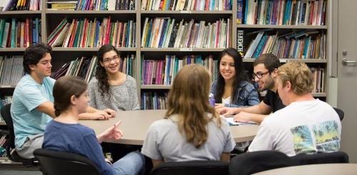 Students gather around a round table in front of a bookshelf.