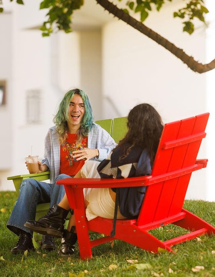 two students sit in adirondack chairs and chat on the mounds