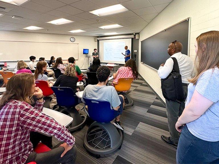 Math conference attendees sitting in a Pitzer classroom as two students present research through a slideshow.